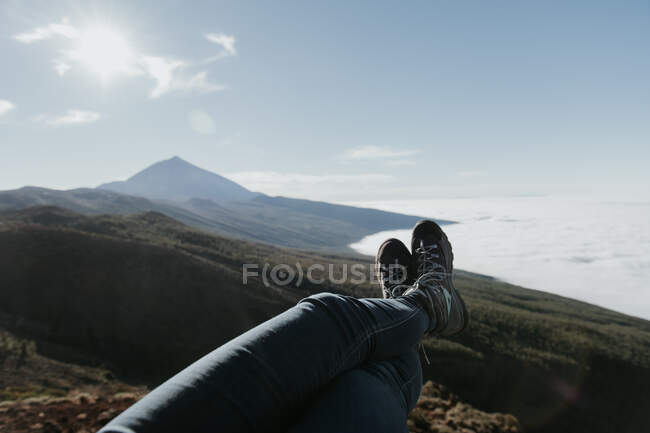 Cultivo piernas de turista irreconocible tumbado y relajante en la cima de la colina - foto de stock