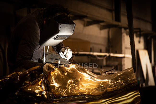 Homem em capacete de solda trabalhando com produto de metal em pouca fundição — Fotografia de Stock