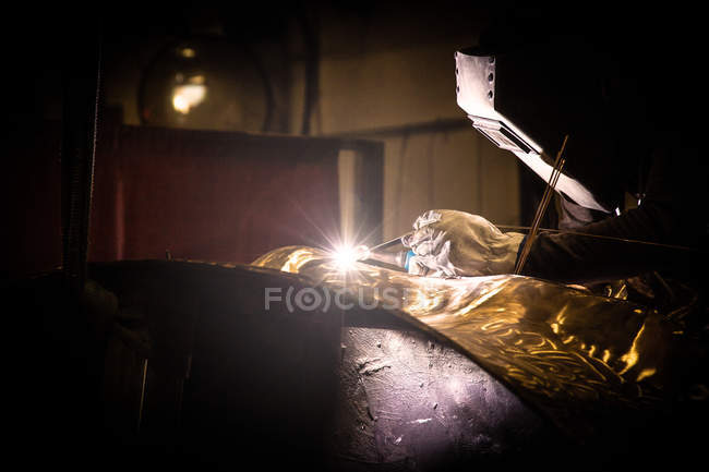 Man in welding helmet working with metal product on little foundry — Stock Photo