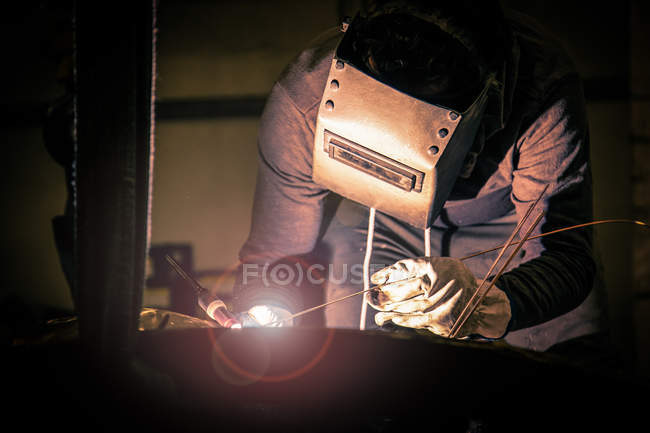Hombre en casco de soldadura que trabaja con producto metálico en pequeña fundición - foto de stock