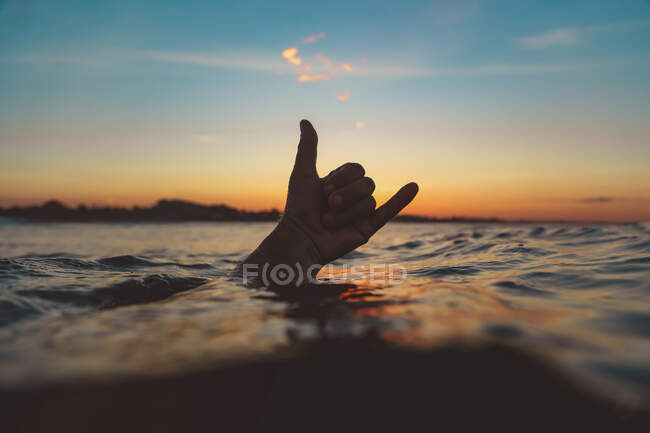 Closeup hand of human showing shaka sign above water surface with ripple and blue heaven in evening on Bali, Indonesia — Stock Photo