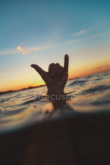Closeup hand of human showing shaka sign above water surface with ripple and blue heaven in evening on Bali, Indonesia — Fotografia de Stock