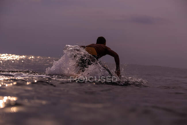 Vista trasera de macho flotando en tabla de surf entre el agua del mar y el cielo nublado en Bali, Indonesia - foto de stock