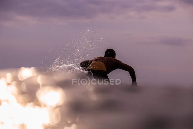 Повернення до зображення чоловіка, який плаває на дошці між водою моря і хмарним небом на Балі (Індонезія). — стокове фото
