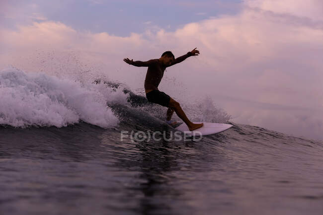 Surf masculin entre les vagues de l'eau de mer avec éclaboussures et ciel nuageux en soirée sur Bali, Indonésie — Photo de stock