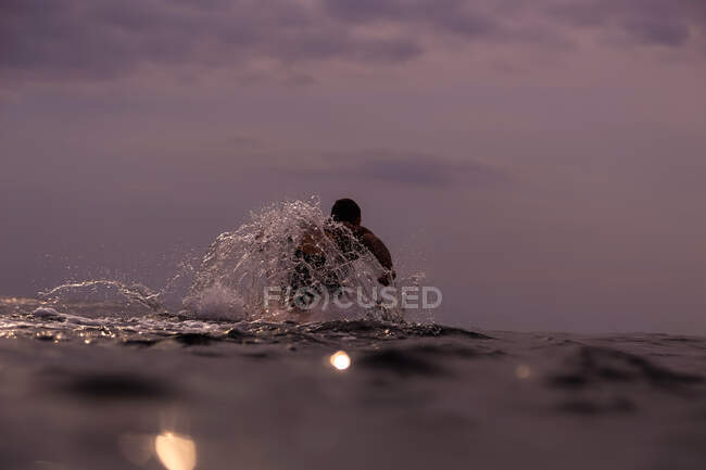 Back view of male floating on surf board between water of sea and cloudy heaven on Bali, Indonesia — Stock Photo