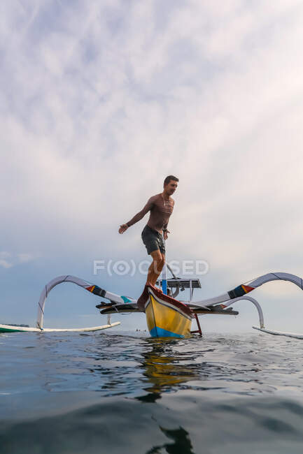 Side view of male jumping from shallop in waving sea and cloudy sky on Bali, Indonesia — Stock Photo