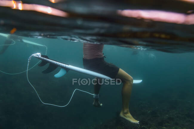 Vista lateral da cultura masculina flutuando na prancha de surf na água azul do mar em Bali, Indonésia — Fotografia de Stock