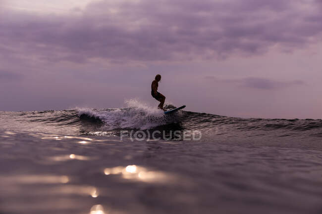 Surfe masculino entre a água ondulante do mar com salpicos e céu nublado à noite em Bali, Indonésia — Fotografia de Stock