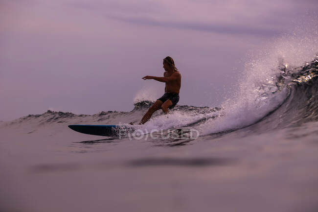 Surf maschile tra acqua di mare ondulata con spruzzi e cielo nuvoloso in serata a Bali, Indonesia — Foto stock