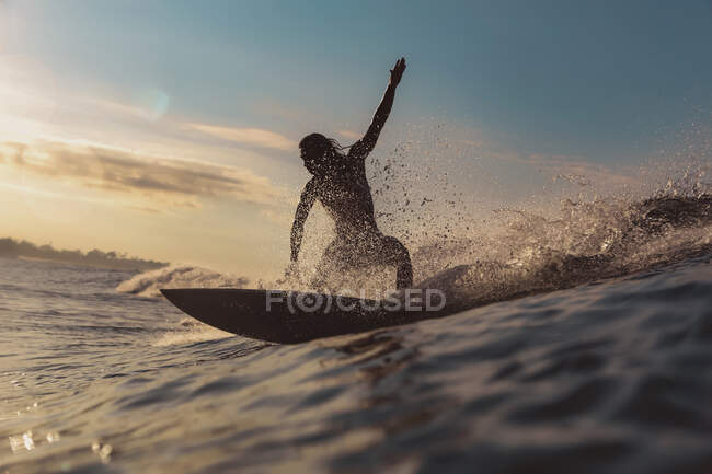 Male surfing between waving water of sea with splashes and cloudy sky in evening on Bali, Indonesia — Stock Photo