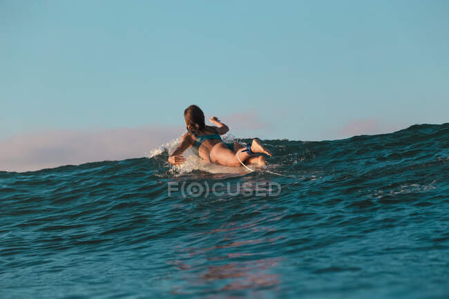 Vue arrière d'une joyeuse femelle flottant sur une planche de surf entre l'eau de mer et le ciel bleu à Bali, Indonésie — Photo de stock