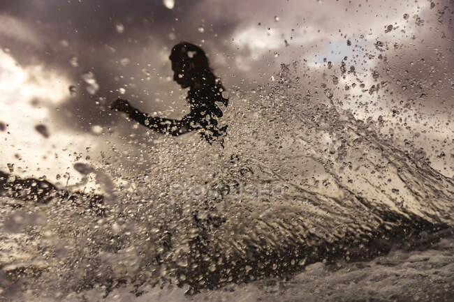 Black and white side view of female floating on surf board between water of sea with splashes on Bali, Indonesia — Stock Photo
