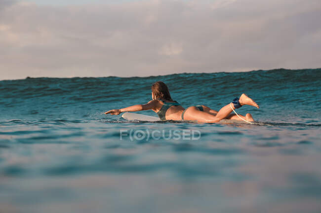 Seitenansicht einer fröhlichen Frau, die auf einem Surfbrett zwischen Meer und blauem Himmel auf Bali, Indonesien, schwimmt — Stockfoto