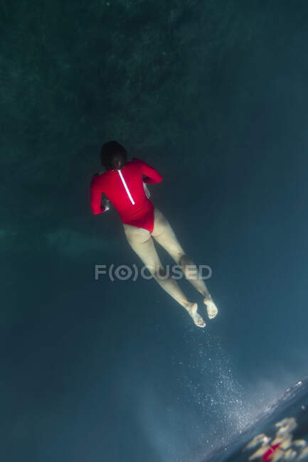 D'en haut femelle en maillot de bain rouge plongeant dans l'eau bleue de la mer à Bali, Indonésie — Photo de stock