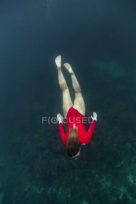 Dall'alto femmina in costume da bagno rosso che si tuffa in acqua azzurra di mare su Bali, Indonesia — Foto stock