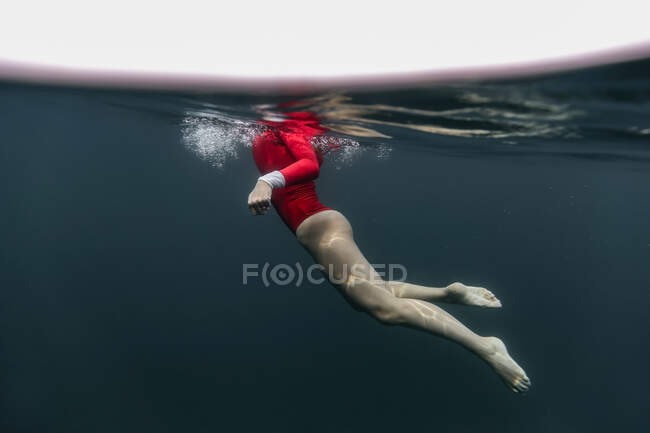 Vista lateral da fêmea em fato de banho vermelho mergulho em água azul do mar em Bali, Indonésia — Fotografia de Stock
