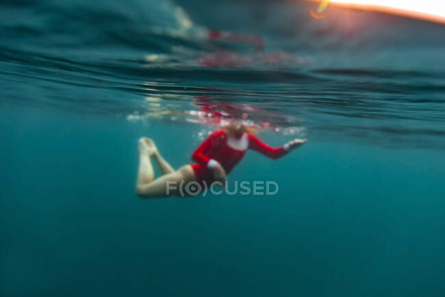 Бічний вид на самицю у червоному купальнику, що пірнає у блакитній воді моря на Балі, Індонезія. — стокове фото