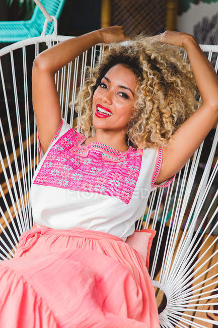 Portrait of happy black young woman with curly hair sitting on wicker chair — Stock Photo