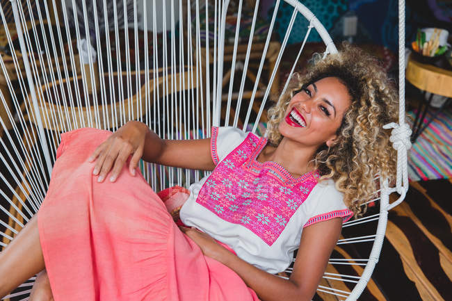 Fröhliche schwarze junge Frau mit geschlossenen Augen und lockigem Haar entspannt auf Korbsessel — Stockfoto