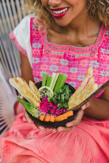 Manos de una joven negra sosteniendo un tazón de verduras frescas - foto de stock