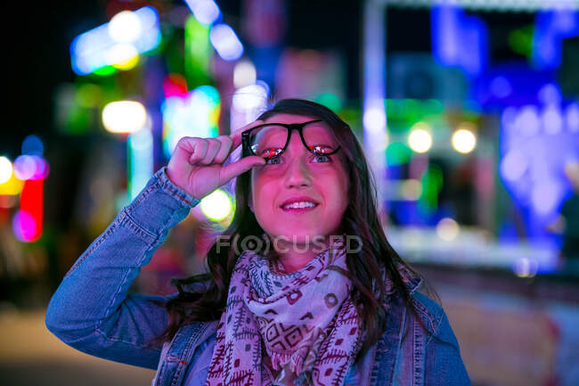 Trendy confident lady in sash and sunglasses near neon lights on street at night on blurred background — Stock Photo