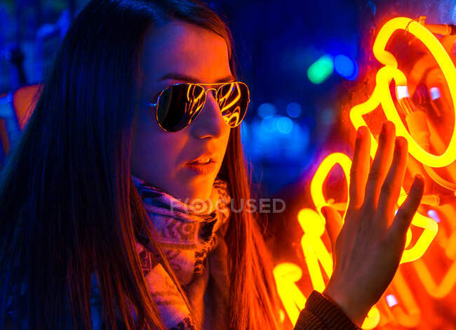 Dame confiante à la mode en ceinture et lunettes de soleil près du mur avec des néons dans la rue la nuit — Photo de stock