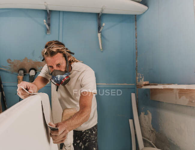 Mann mit Atemschutzmaske misst Surfbrett in Werkstatt — Stockfoto