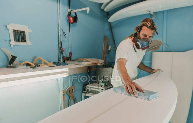 Männchen in Verschnaufpause mit Schleifpapier polieren Holz Surfbrett am Arbeitsplatz — Stockfoto