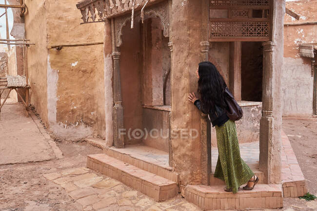 Vista lateral de la joven dama de pie cerca del edificio retro en la calle en Marrakech, Marruecos - foto de stock