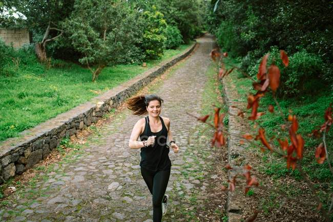 Happy woman in sportswear running on pathway in park — Stock Photo