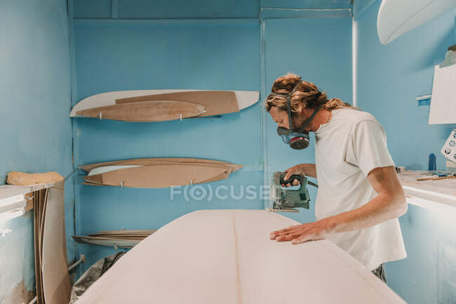 Homem com ferramenta de serrar prancha de surf na oficina — Fotografia de Stock