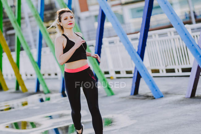 Woman in sportswear with earphones and smartphone running on street — Stock Photo