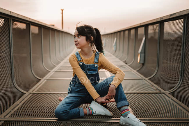 Дівчина сидить на скейтборді на металевому мосту і дивиться геть — стокове фото