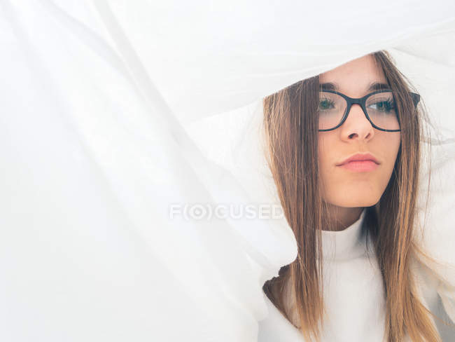 Orgulloso adolescente en gafas y desgaste blanco mirando hacia otro lado entre cortinas de luz - foto de stock