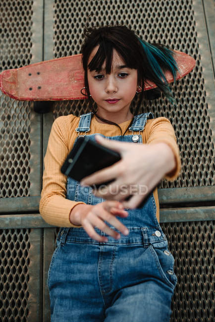 Mädchen mit Smartphone und Skateboard auf Metallsteg liegend — Stockfoto