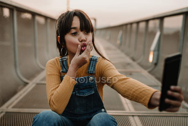 Menina engraçada tomando selfie com smartphone na ponte de metal — Fotografia de Stock