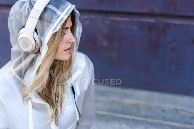 Nachdenklich stilvolle Frau im Regenmantel mit Kopfhörern auf dunklem Hintergrund — Stockfoto