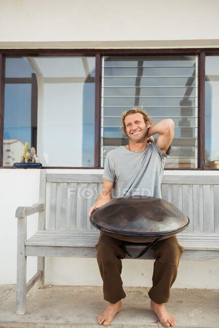 Homme blond assis sur un banc avec un gros tambour à main — Photo de stock