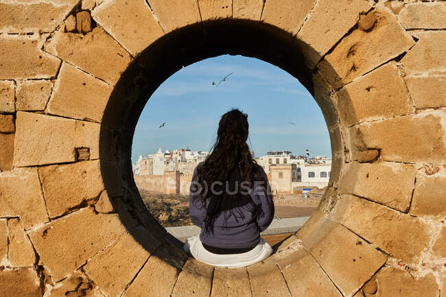 Back view of young brunette lady sitting on rock monument near old town in Marrakesh, Morocco — Stock Photo