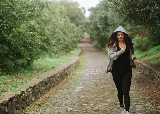 Positive woman in sportswear running on pathway in park — Stock Photo