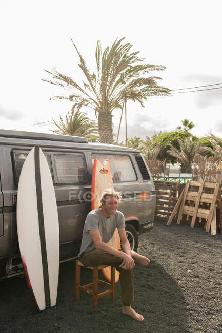 Человек, стоящий возле досок для серфинга и фургона — стоковое фото