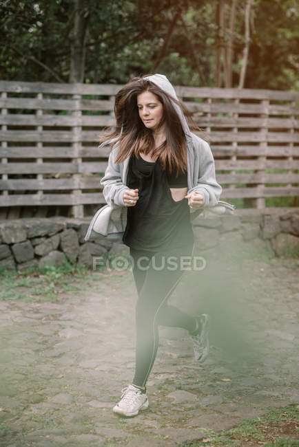 Уверенная в себе женщина в спортивной одежде, бегающая возле деревянного забора в сельской местности — стоковое фото
