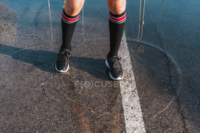 Imagen recortada de las piernas de la señora en legwarmers y zapatillas de correr de pie en charco sobre asfalto - foto de stock