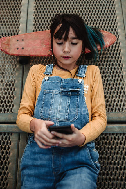 Дівчина зі смартфоном і скейтбордом лежить на металевій доріжці — стокове фото