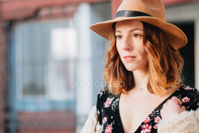Mujer joven atractiva positiva en vestido con un sombrero mirando hacia otro lado - foto de stock