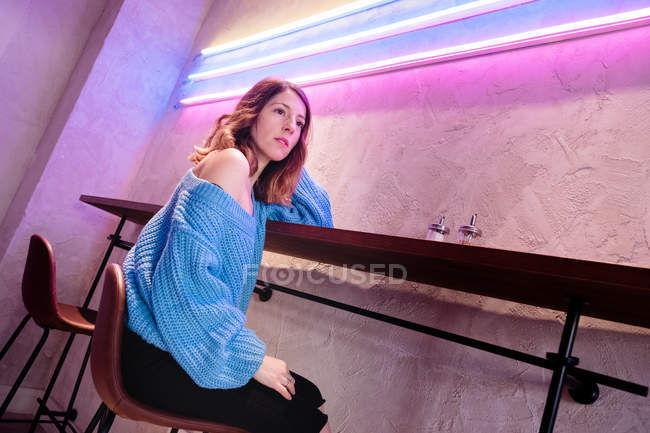 Positive Frau mit Tasse am Tisch neben Wand mit Neonlampen — Stockfoto