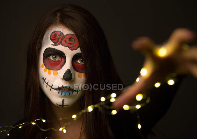 Jovem com pintura facial assustadora segurando luzes de fadas — Fotografia de Stock