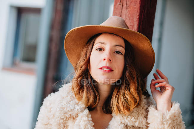 Mujer joven atractiva positiva en el desgaste cálido y sombrero mirando a la cámara - foto de stock