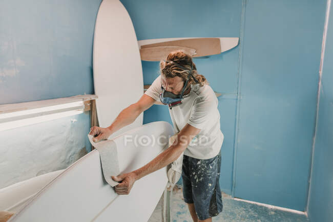 Hombre en respirador midiendo tabla de surf en taller - foto de stock